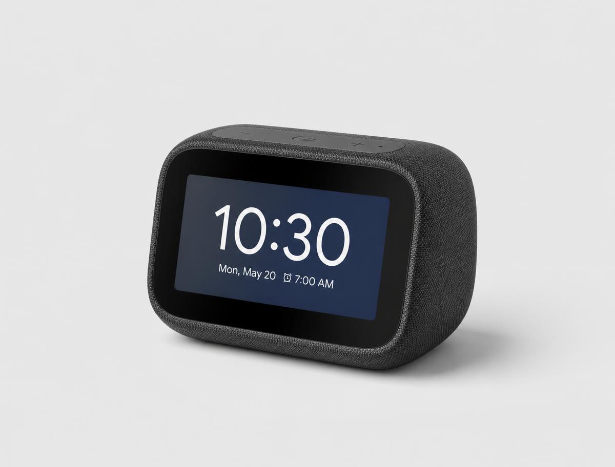 Small round smart alarm clock display on a wooden nightstand beside a bed